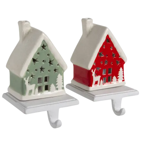 Two ceramic house-shaped stocking holders, one in green and one in red, featuring star cutouts and festive deer and tree designs, each with a hook for hanging.