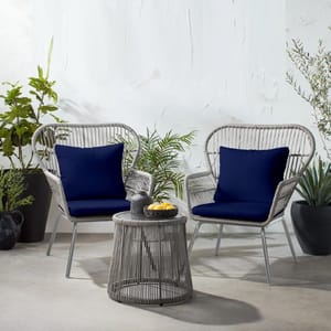 Two grey wicker chairs with blue cushions, accompanied by a grey round wicker table, surrounded by potted plants.