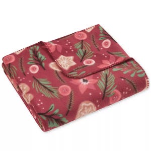 A red fleece blanket with a festive design featuring pine branches, pink flowers, and stars.