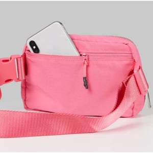 A pink waist bag with a smartphone peeking out of its open compartment.