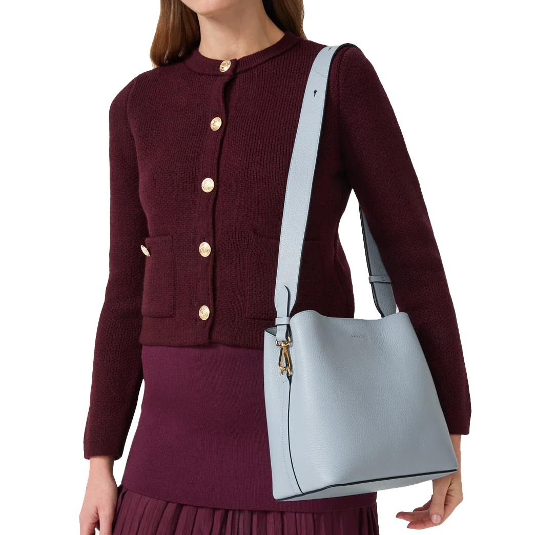 A person is wearing a dark burgundy cardigan with gold buttons and a matching skirt, holding a light blue leather shoulder bag with a wide strap.