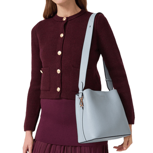 A person is wearing a dark burgundy cardigan with gold buttons and a matching skirt, holding a light blue leather shoulder bag with a wide strap.