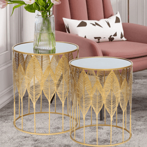 Set of 2 gold-toned nesting end tables with a decorative leaf pattern and mirrored tops, shown next to a pink chair and pillow.