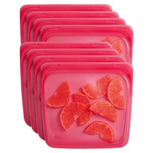 Reusable food storage bags are pink, silicone, and feature a clear portion to view contents. They contain orange slices and are designed for airtight storage, ideal for preserving freshness.