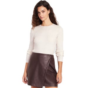 A woman is wearing a cream-colored ribbed sweater with long sleeves and a dark brown leather mini skirt that has a wrap design.