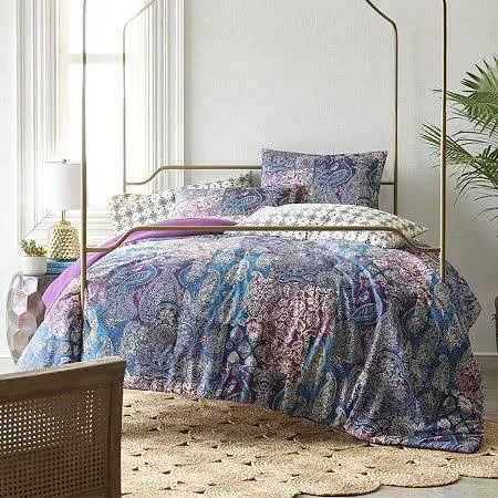 A bed with paisley patterned bedding, including pillows, shams, and a comforter in shades of purple, pink, and blue.