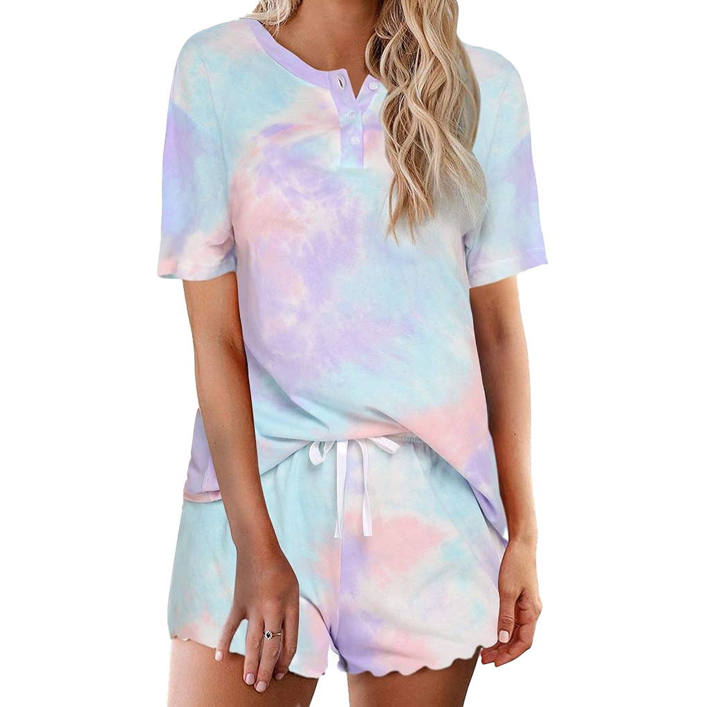 Tie-dye loungewear set featuring a short-sleeve top with button details and matching drawstring shorts in pastel shades of blue, pink, and lavender.
