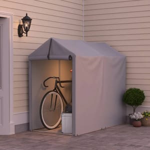 A compact, gray portable storage shed is attached to a house wall, housing a bicycle, helmet, and a white box. It's constructed with a fabric covering and has a peaked roof design.