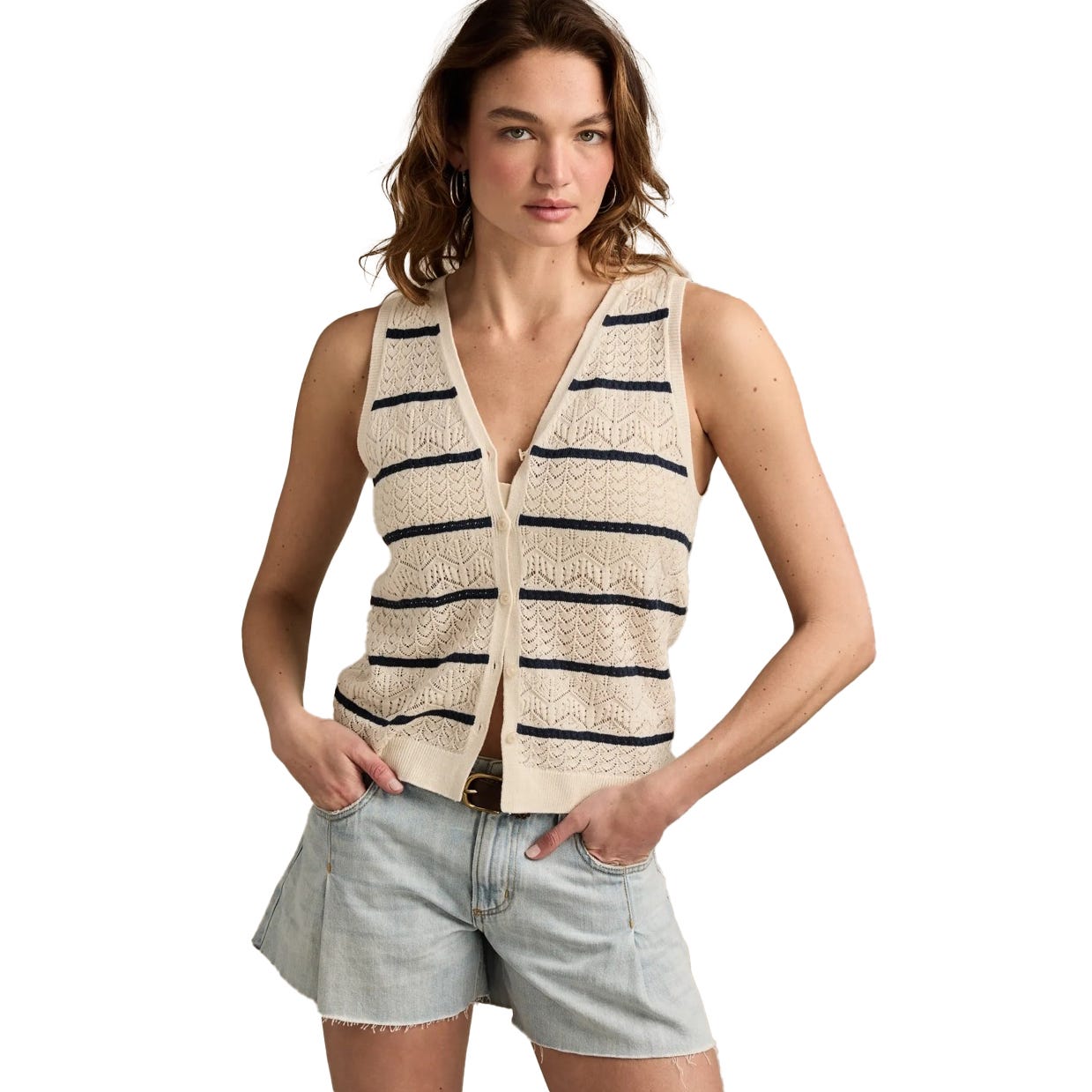 A woman is wearing a sleeveless, button-front knit vest with navy stripes over a white top, paired with light denim shorts.