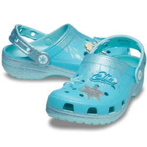 Light blue Crocs featuring a \“Frozen\“ theme with glittery details, snowflakes, and the name \“Elsa\“ on the top.