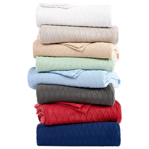 A stack of soft blankets in various colors, including white, beige, green, blue, grey, red, and navy, each with a diamond pattern design.