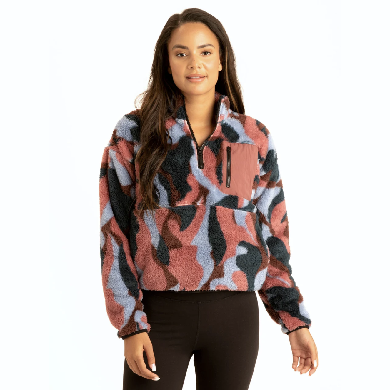 A woman wears a colorful, patterned fleece pullover with a half-zip and zippered chest pocket, paired with black leggings.
