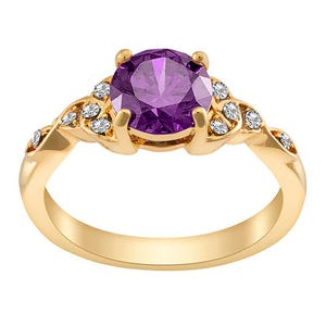 A gold ring featuring a central round purple gemstone, flanked by clusters of small clear stones on a delicately embellished band.