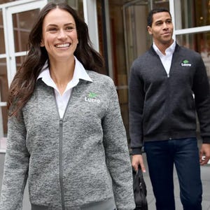 Two people wear grey fleece jackets with a company logo on the chest.