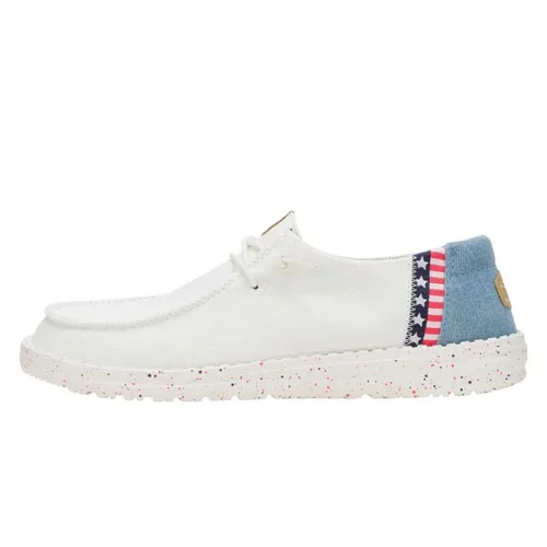 Hey Dude Wendy Americana Shoes feature a white canvas upper with a blue and star-striped heel detail, speckled white outsole, and a relaxed slip-on design with laces for a casual, patriotic look.