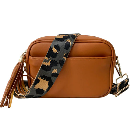 A tan crossbody bag with a large front pocket, gold hardware, and a tassel accent. It features a detachable strap with a black and tan animal print design.