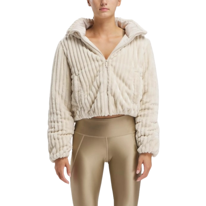 A woman is wearing a cropped, cream-colored Reebok puffer jacket with a textured, ribbed design and a hood, paired with coordinating leggings.
