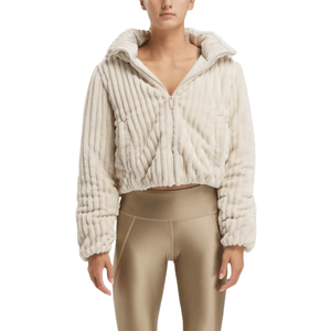 A woman is wearing a cropped, cream-colored Reebok puffer jacket with a textured, ribbed design and a hood, paired with coordinating leggings.