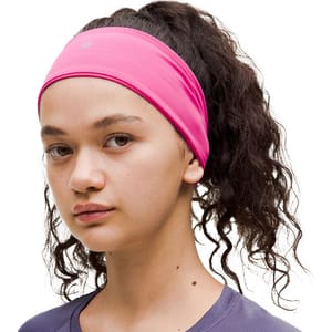 A pink headband with a small circular logo on the front, designed to keep hair in place during workouts.