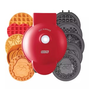 A red, circular Dash waffle maker with interchangeable plates to create different holiday-themed waffles, including patterns like snowflakes and gingerbread men.