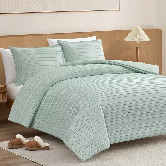 A bedroom setting featuring a light green textured duvet cover with matching pillow shams on a wooden bed frame, accompanied by a pair of plush slippers on a light rug.
