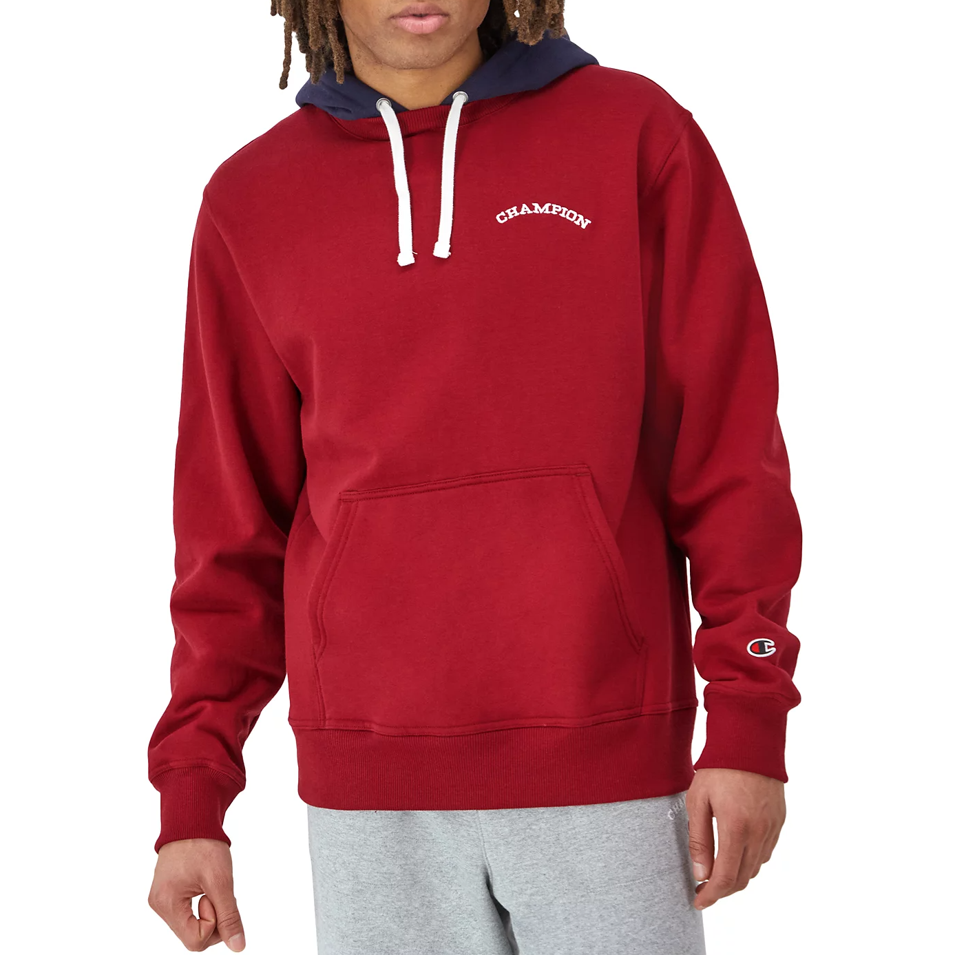 Red Champion hoodie with a kangaroo pocket and white drawstrings, featuring the Champion logo on the chest and sleeve. The hood has a contrasting dark interior, and it's paired with light gray sweatpants.