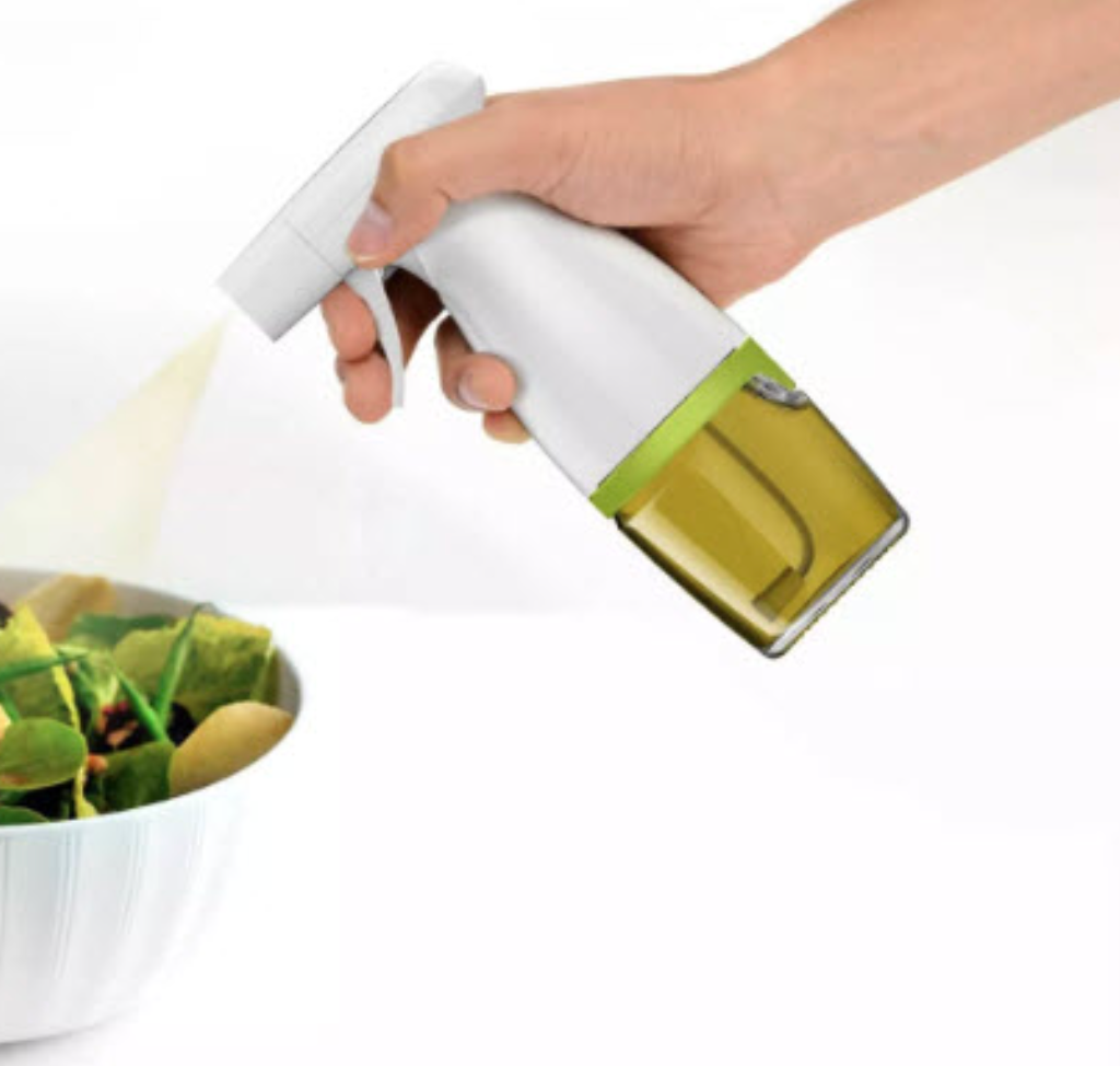 A person is spraying a salad with a handheld oil sprayer, which has a white handle and a transparent section for the oil.
