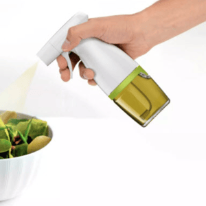 A person is spraying a salad with a handheld oil sprayer, which has a white handle and a transparent section for the oil.