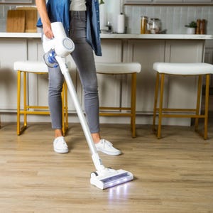 A person is using a cordless stick vacuum cleaner on a hardwood floor.