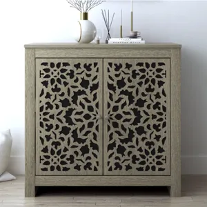 A decorative wooden cabinet with intricate floral cut-out patterns on its doors, placed in a minimalistic room setting with a vase, candles, and books on top.