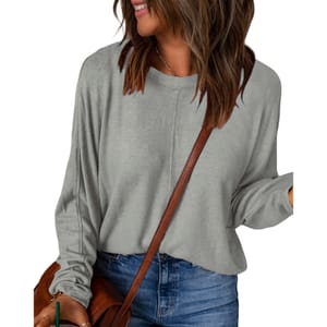 A woman is wearing a loose-fitting, long-sleeved gray top with a round neckline, paired with blue jeans and a brown crossbody strap.