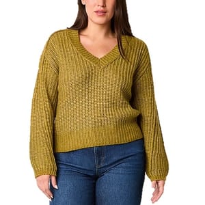 A woman wearing a mustard yellow V-neck sweater with a textured knit pattern and long sleeves, paired with blue jeans.