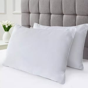 Two white pillows on a bed with a tufted grey headboard in the background, accompanied by a white vase with tulips.