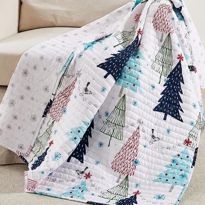 A quilt with a Christmas tree and snowflake pattern draped over a couch.