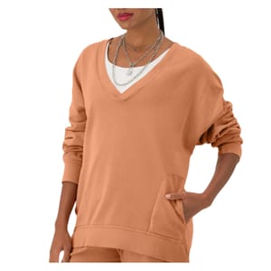A person wearing a tan V-neck sweater with layered necklaces and pockets.
