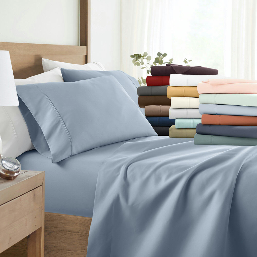 The 6pc Sheet Sets feature multiple colors with a soft, smooth appearance, including blue, peach, burgundy, white, and beige. Displayed on a bed and in a stacked pile, they suggest a variety of colors for selection.