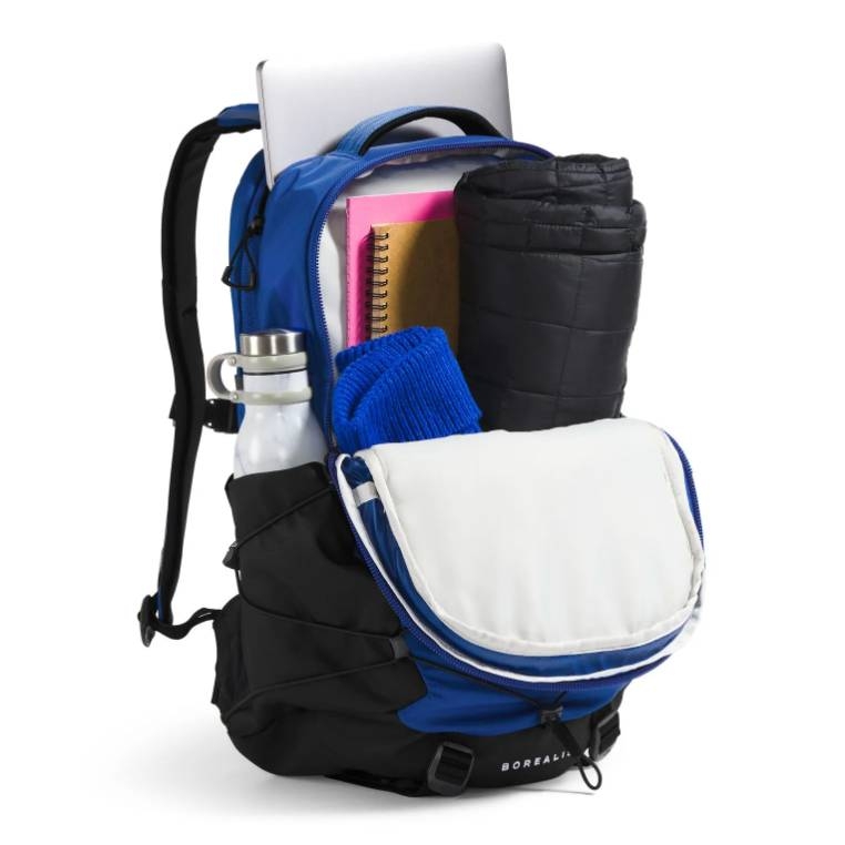 A blue and black North Face Borealis Backpack is shown packed with items including a laptop, a water bottle, a notebook, a rolled-up jacket, and a blue garment.