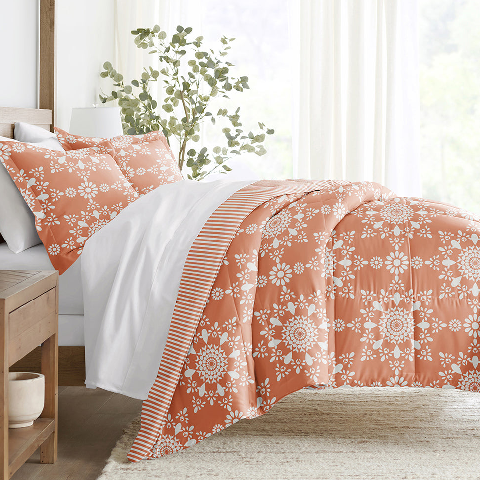 Orange and white floral duvet cover with matching pillowcases, featuring a striped lining, on a neatly made bed beside a wooden nightstand and a potted plant, in a well-lit bedroom.