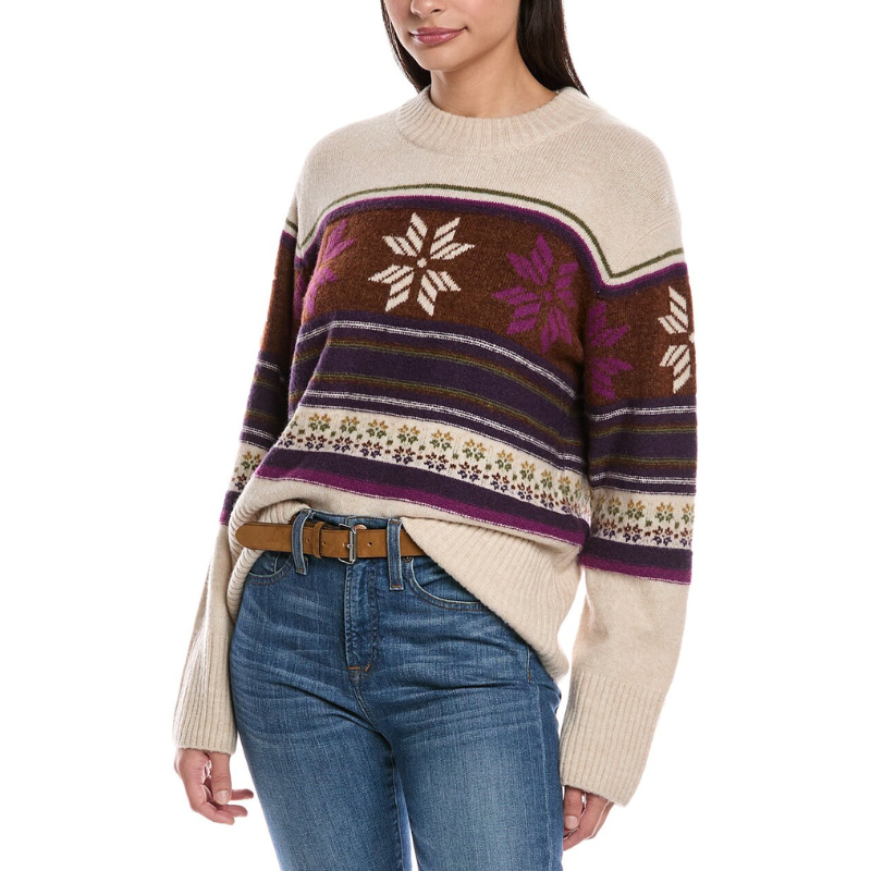 A woman is wearing a cozy knit sweater with a snowflake and stripe pattern, paired with blue jeans and a brown belt.