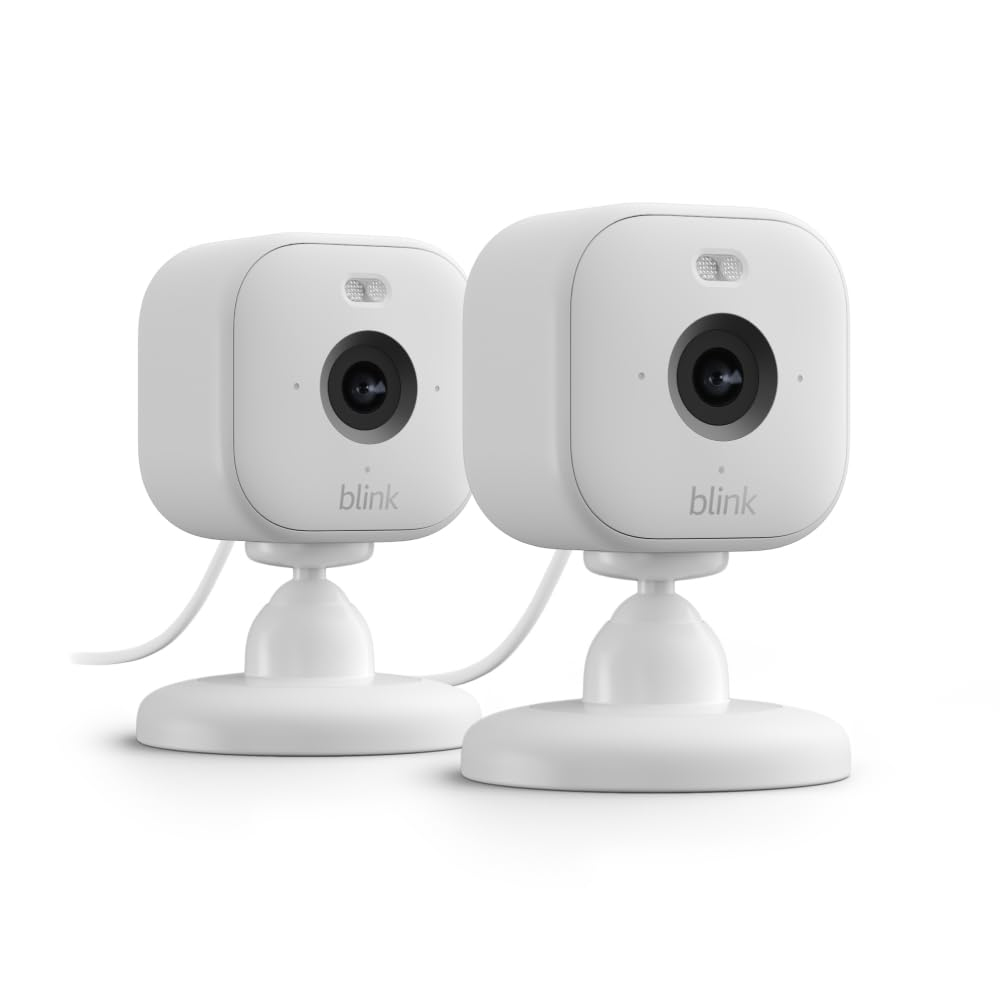 The 2pk Blink Mini Cameras are compact, white indoor security cameras designed for easy installation, featuring HD video, motion detection, and two-way audio. They rest on adjustable stands for flexible positioning and require a power source via cable.