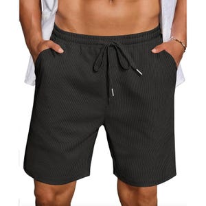 Black drawstring shorts with a subtle textured pattern, worn by a person with hands in pockets. Casual style.