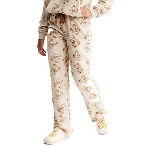 A cozy outfit featuring cream-colored pajamas with a teddy bear pattern, paired with matching slippers that have a teddy bear design on the front.