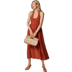 J.Crew Halter Mixy Dress features a rust-colored halter neckline with a fitted bodice and an A-line skirt. Accessorized with a woven clutch adorned with white embellishments, gold bangles, and red sandals.