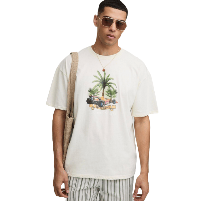 A man is wearing a beige graphic t-shirt featuring palm trees and a car, striped shorts, sunglasses, and a shoulder bag.