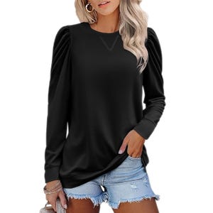 A woman is wearing a black long-sleeve top with puff sleeves and blue distressed denim shorts. She accessorizes with large hoop earrings and several bracelets.