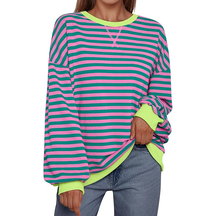 The oversized striped sweatshirt features green and pink horizontal stripes, with neon green cuffs and collar. It's styled with loose, long sleeves and is paired with blue jeans.