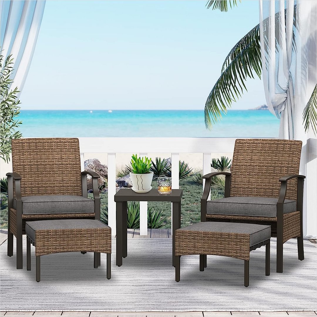 Outdoor furniture set with two wicker chairs, two ottomans, and two side tables on a patio overlooking the sea.