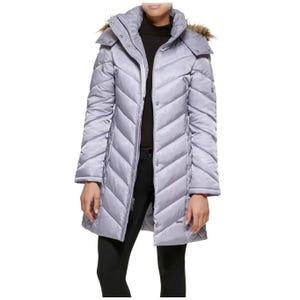 A silver-grey, knee-length women's puffer coat by Kenneth Cole features diagonal quilting, a high collar, zip closure, and a faux fur-trimmed hood, offering a sleek, insulated design for cold weather.