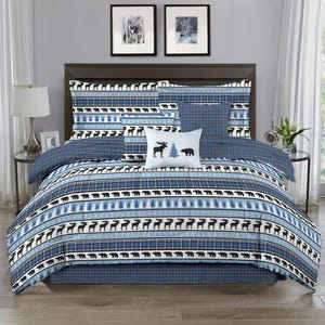 Bedding set featuring a rustic theme with patterns of bears and trees on a blue and white background, including a comforter, pillows, and shams, complemented by a plaid design.