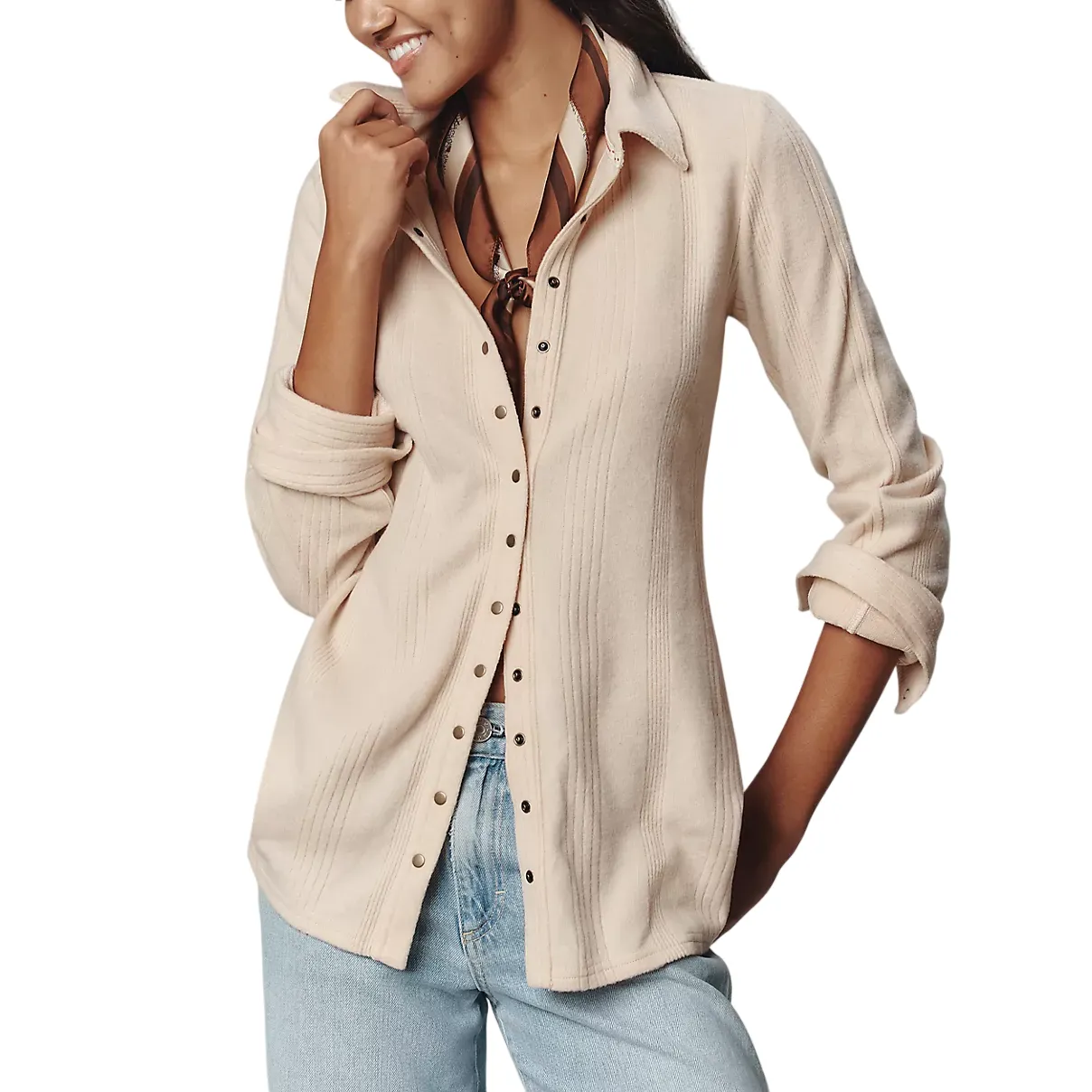 A model wears a light beige button-up shirt with a ribbed texture, paired with light blue jeans. She accessorizes with a brown and cream scarf around her neck.